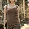 Woman wearing a brown tank top and pants standing in front of stone ruins.