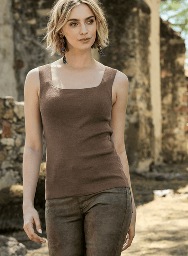 Woman wearing a brown tank top and pants standing in front of stone ruins.